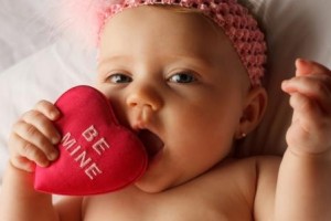 Baby chewing on a heart pillow embroidered with "Be Mine"