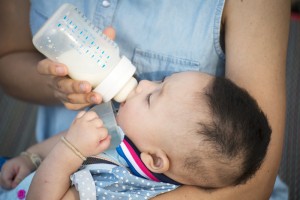 Baby drinking bottle in woman's arms